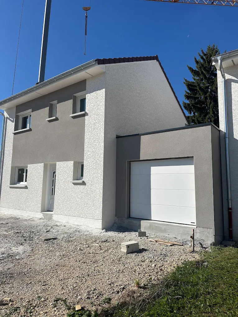 Maison à enduit gris avec détails clairs autour des fenêtres et garage attenant